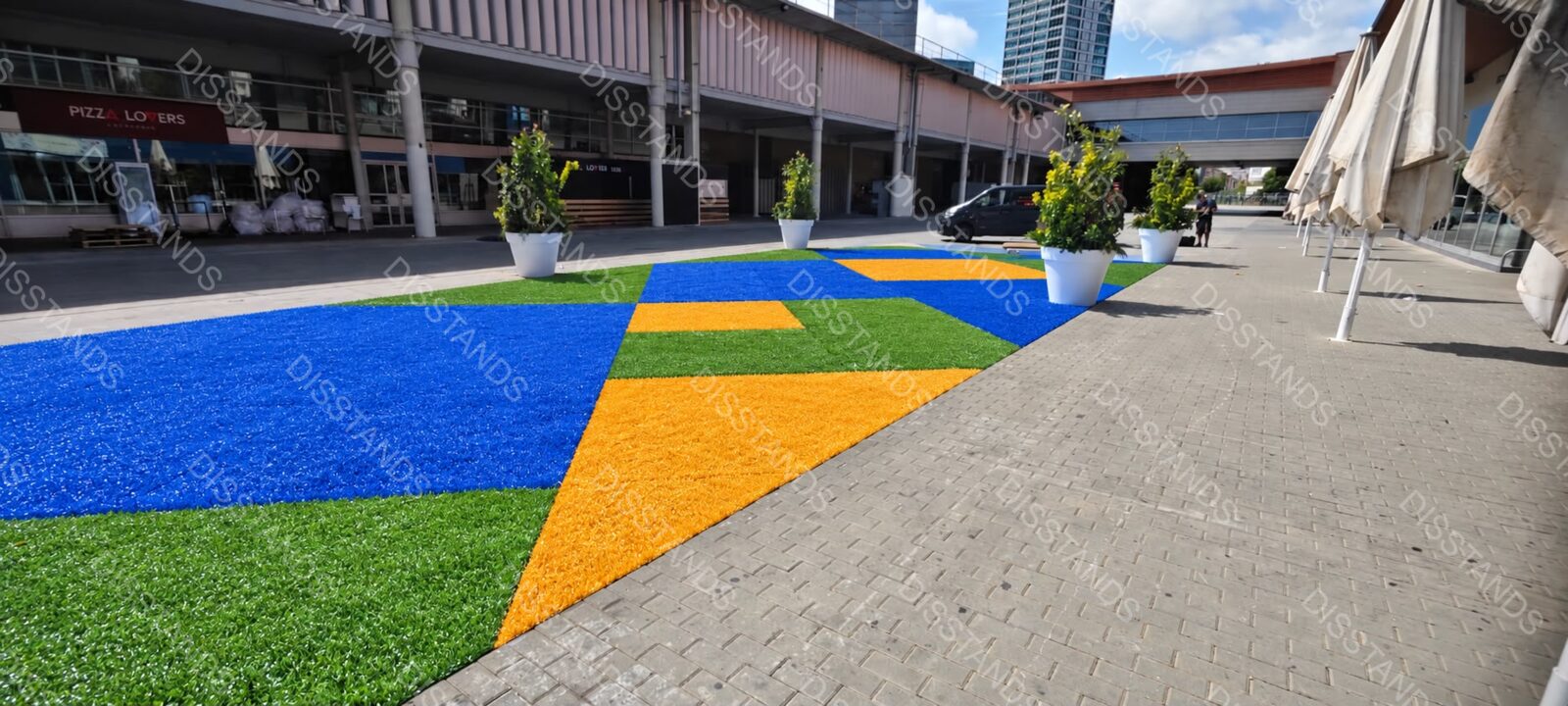 Césped Pradis 25MM - Azul, amarillo y verde en una plaza